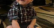 Lucas is registered to the contest to win money with this photo: baby, child, plaid_shirt, shorts, sitting, carpet, indoor, furniture, bed, happy, smiling, person, foot, hand, curly_hair, cute, young, portrait, infant, casual_clothing