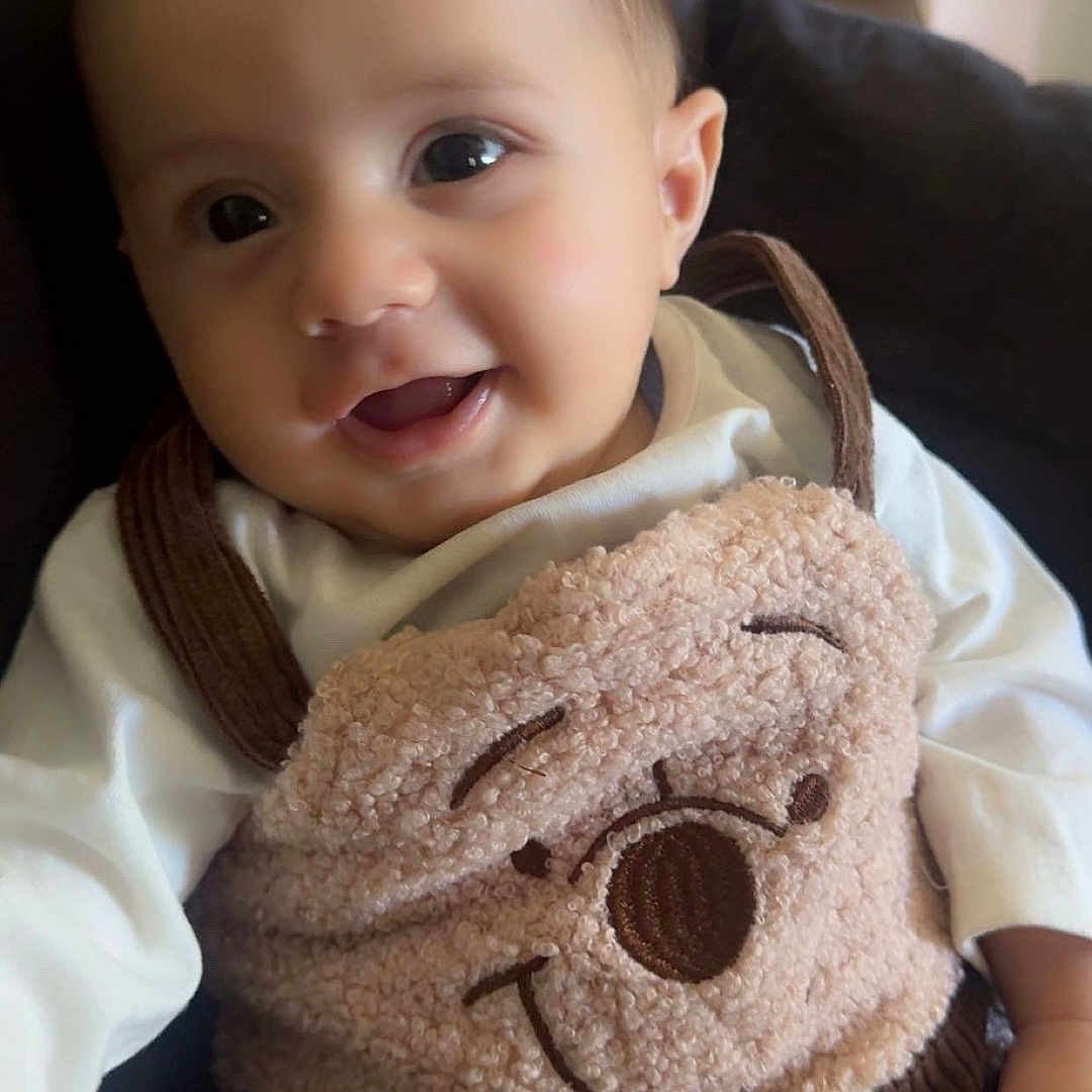 Amir is registered to the contest to win money with this photo: baby, child, infant, smiling, portrait, indoor, seated, teddy_bear, stuffed_animal, plush_toy, cuddling, white_clothing, brown, cozy, chair, close_up, face, happy, home, photography