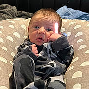 Dayton is registered to the contest to win money with this photo: baby, infant, onesie, camo_pattern, pillow, indoor, face, hand, expression, curious, comfort, resting, child, human, portrait, cozy, soft_lighting, casual, young, cute