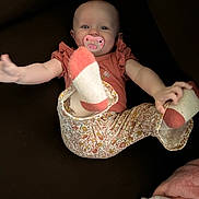 Harper joined the competition — help win amazing prizes! baby, child, pacifier, socks, floral_pants, ruffled_top, smiling, face, hands, feet, indoor, blanket, cozy, playful, happy, person, infant, cute, portrait, clothing