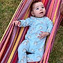 baby, infant, onesie, rainbow_pattern, hammock, striped_hammock, grass, outdoor, hand, footwear, shoe, curious, blue_eyes, relaxing, person, child, fabric, colorful, casual, playful