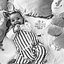 baby, infant, smiling, striped_clothing, plush_toys, cushion, playmat, hand_in_mouth, happy, lying_down, monochrome, face, foot, soft_toys, child, comfortable, indoors, cute, portrait, cozy