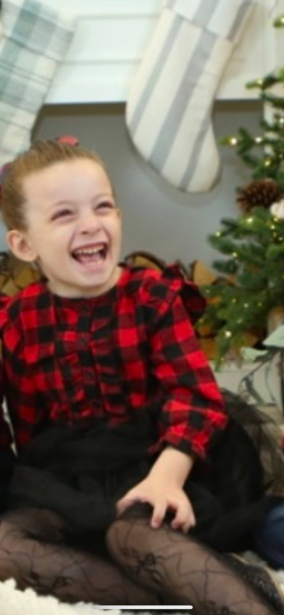 Nataly is registered to the contest to win money with this photo: child, christmas_tree, conifer, dress, event, flooring, fun, happy, holiday, holiday_ornament, human_body, ornament, pattern, person, plaid, room, sitting, sleeve, smile, tartan