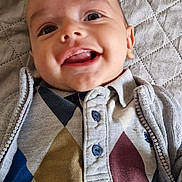 élys participe au concours pour gagner de l'argent avec cette photo : baby, smiling, face, child, clothing, argyle, quilted_blanket, happy, portrait, cute, young, infant, buttoned_shirt, sweater, lying_down, indoors, closeup, person, head, expression