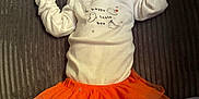 Raya is registered to the contest to win money with this photo: baby, sleeping, pacifier, orange_tutu, orange_pants, white_shirt, ghost_print, cozy, blanket, soft_toys, cute, infant, child, indoors, resting, peaceful, clothing, footwearless, lying_down, toddler