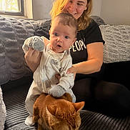 Raya is registered to the contest to win money with this photo: baby, woman, cat, indoor, couch, pajamas, smiling, pet, furniture, person, animal, child, cozy, window, blanket, hand, hair, face, living_room, curious