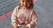 Emberlyn is registered to the contest to win money with this photo: child, toddler, smiling, outdoor, sidewalk, concrete, pigtails, red_bows, cards, street, curb, casual_clothing, sweatshirt, pants, sneakers, sunlight, happy, young_child, person, standing