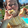 blue_sky, child, clouds, daytime, dress, face, food, girl, grass, hand, outdoor, park, person, picnic, pigtails, sandwich, smile, sunlight, tree, yellow