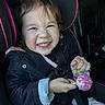 child, toddler, car_seat, smile, happy, face, jacket, hair, cake_pop, sprinkles, hand, seatbelt, vehicle_interior, playful, cute, person, indoors, colorful, fun, joy