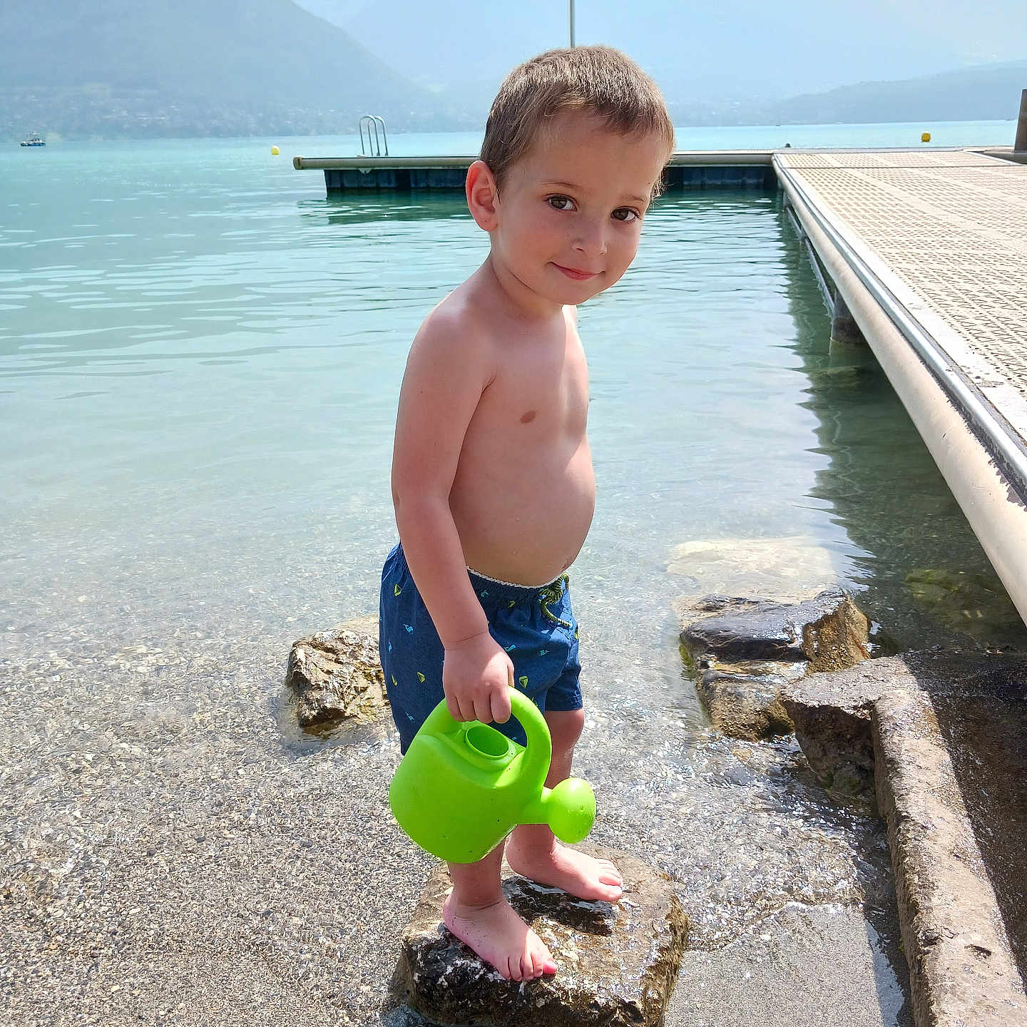 Timeo participe au concours pour gagner de l'argent avec cette photo : barefoot, boy, child, daylight, happy, lake, mountains, nature, outdoor, play, recreation, rock, scenic, shore, summer, swimming_trunks, vacation, water, watering_can, young