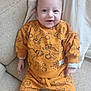 Lowen a rejoint le concours — aidez-le/la à gagner de superbes lots ! baby, infant, smile, orange_clothing, lion_cub_pattern, couch, blanket, happy, child, sitting, cute, indoors, portrait, young_child, cozy, soft_fabric, socks, hand, face, head
