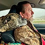 Bella is registered to the contest to win money with this photo: man, dog, brindle_dog, car_interior, driver, camouflage_jacket, head_rest, window, shoulder, companion, pets, vehicle, road_trip, affection, seat, beard, patterned_bag, leather_seat, side_profile, foggy_weather