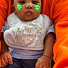 baby, child, infant, bib, clothing, orange_sweater, sitting, cute, face_filter, digital_sticker, green_dinosaur, hands, legs, socks, portrait, indoor, person, holding, expressionless, casual