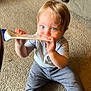 baby, child, carpet, blue_eyes, sitting, tube, chewing, clothing, pants, shirt, indoor, furniture, baby_gate, curious, floor, foot, hand, face, young_child, home
