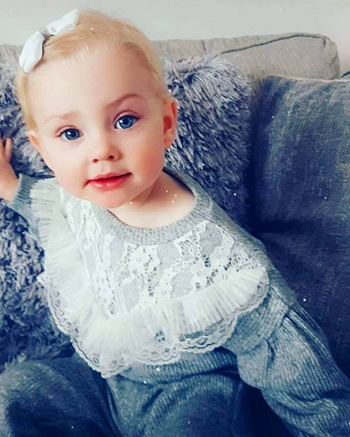 Maisy joined the competition — help win amazing prizes! baby, baby_toddler_clothing, blond, cheek, child, child_model, couch, day_dress, denim, embellishment, eye, hair_accessory, iris, living_room, person, portrait_photography, sitting, skin, toddler