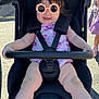 baby, sunglasses, stroller, outdoor, smile, child, sunny, happy, seatbelt, legs, clothing, footwear, black, pink, person, babywear, sunshade, road, toy, cute
