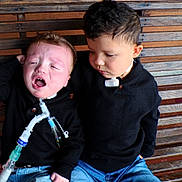 Bryant is registered to the contest to win money with this photo: child, children, crying, medical_tube, breathing_tube, bench, wooden_bench, black_clothing, jeans, sitting, concern, emotion, indoor, people, face, young, healthcare, support, casual_clothing, portrait