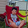 Weston is registered to the contest to win money with this photo: child, boy, red_chair, outdoor, sunny_day, blue_sky, clouds, grass, concrete, chain_link_fence, bib, shorts, tshirt, smiling, curly_hair, backyard, relaxed, casual, daylight, person