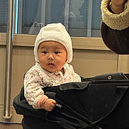 Tara participe au concours pour gagner de l'argent avec cette photo : baby, child, stroller, hat, indoor, hand, clothing, face, person, infant, cozy, grip, curious, toddler, floral, black, adult_hand, window, reflection, floor