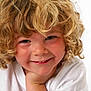 child, curly_hair, smile, face, portrait, white_shirt, blond, happy, close_up, hand, cheek, cute, young, innocent, person, light_background, skin, blue_eyes, head, expression
