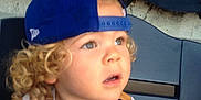 Ashton joined the competition — help win amazing prizes! child, toddler, curly_hair, baseball_cap, blue_cap, sports_jersey, stadium_seat, looking_up, outdoor, young_child, casual_clothing, blond_hair, portrait, seat_back, curious_expression, daylight, person, hat, captured_moment, baseball
