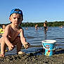 toddler, child, blue_cap, sand, mud, bucket, paw_patrol, water, lake, outdoor, summer, playing, barefoot, wet, people, background, nature, sunny, recreation, reflection