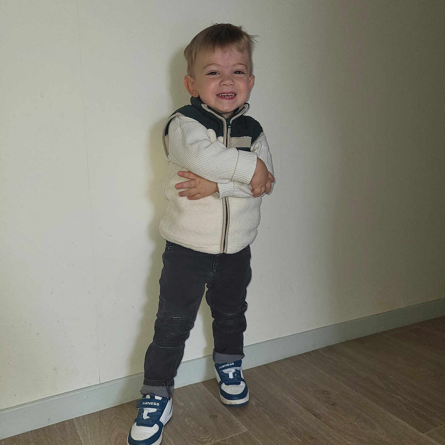 Aydenn participe au concours pour gagner de l'argent avec cette photo : blue_sneakers, casual_clothing, child, cute, dark_pants, fashion, feet, flooring, footwear, happy, indoor, person, plain_wall, portrait, smiling, standing, toddler, white_jacket, wooden_floor, young