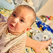 Zorawar is registered to the contest to win money with this photo: adult_foot, baby, bed, bib, blanket, child, closeup, clothing, colorful, curious, eyes, face, indoor, infant, nursery, portrait, sitting, smiling, striped_shirt, toys