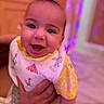 Zorawar joined the competition — help win amazing prizes! adult_hand, baby, bib, blue_clothing, child, close_up, colorful_lighting, face, family, happy, held, indoors, infant, pink_lighting, portrait, purple_lighting, short_sleeves, smiling, wooden_background, yellow_clothing