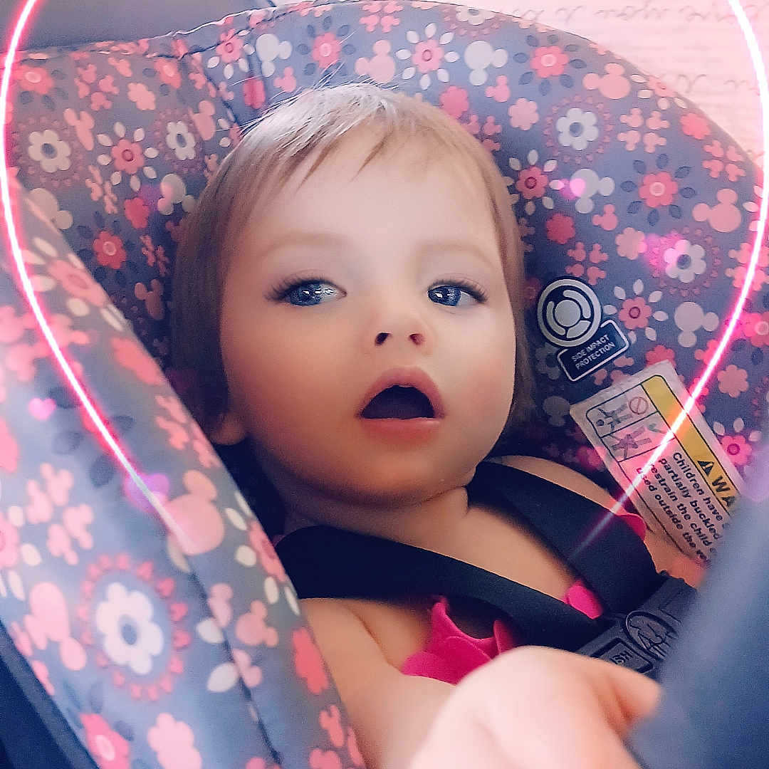 Willow is registered to the contest to win money with this photo: baby, blue_eyes, car_seat, child, closeup, cute, expression, face, floral_pattern, hand, indoor, mickey_mouse, neon_heart, pink_clothing, portrait, safety_label, seat, seatbelt, toddler, vehicle_interior