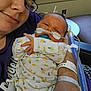 Jeremiah is registered to the contest to win money with this photo: baby, newborn, pacifier, oxygen_tube, hospital, adult, glasses, onesie, animal_print, window, medical_equipment, arm_band, person, holding, close_up, indoor, smile, care, healthcare, bedroom