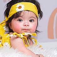 Amanat is registered to the contest to win money with this photo: baby, child, infant, yellow_headband, yellow_outfit, daisy_pattern, fluffy_surface, curly_hair, big_eyes, cute, portrait, closeup, soft_lighting, indoor, skin, person, headband, expression, baby_girl, adorable