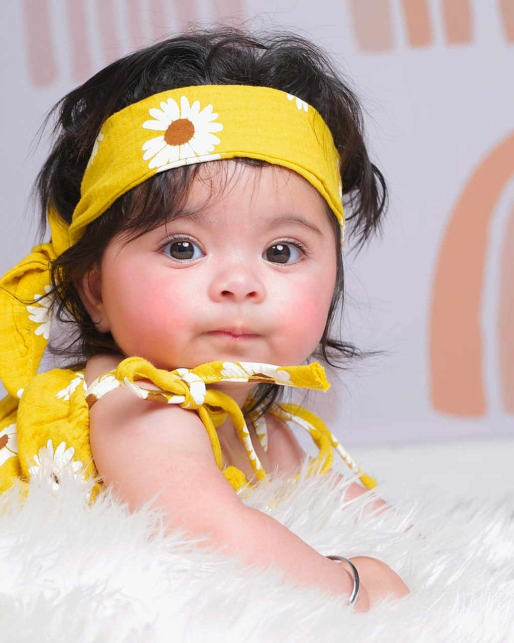 Amanat is registered to the contest to win money with this photo: baby, child, infant, yellow_headband, yellow_outfit, daisy_pattern, fluffy_surface, curly_hair, big_eyes, cute, portrait, closeup, soft_lighting, indoor, skin, person, headband, expression, baby_girl, adorable