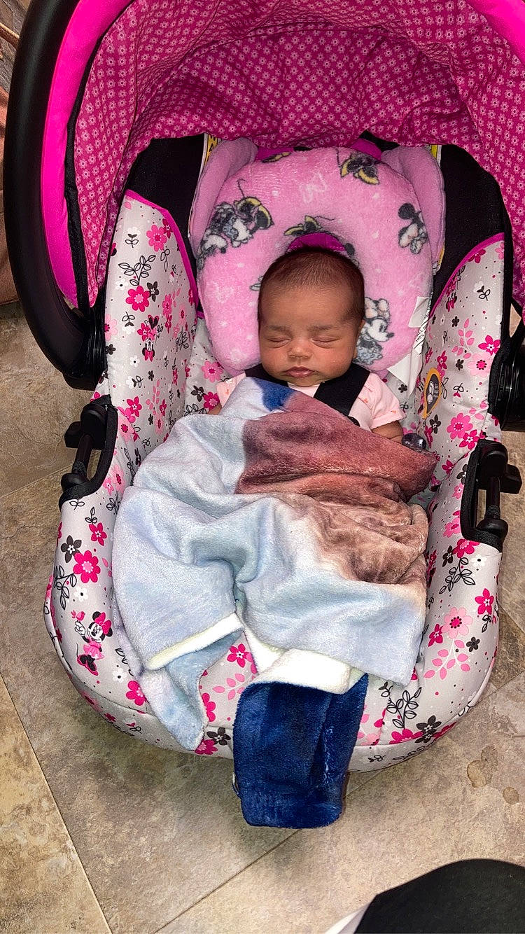 Alora is registered to the contest to win money with this photo: baby, baby_carriage, baby_products, baby_sleeping, baby_toddler_clothing, cheek, child, comfort, headgear, lap, magenta, outerwear, pattern, person, pink, product, sitting, sleeve, textile, toddler