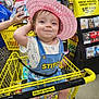 toddler, child, shopping_cart, hat, pink_hat, clothing, store, shopping, yellow, dollar_general, smiling, face, person, retail, aisle, socks, cute, happy, indoor, overalls