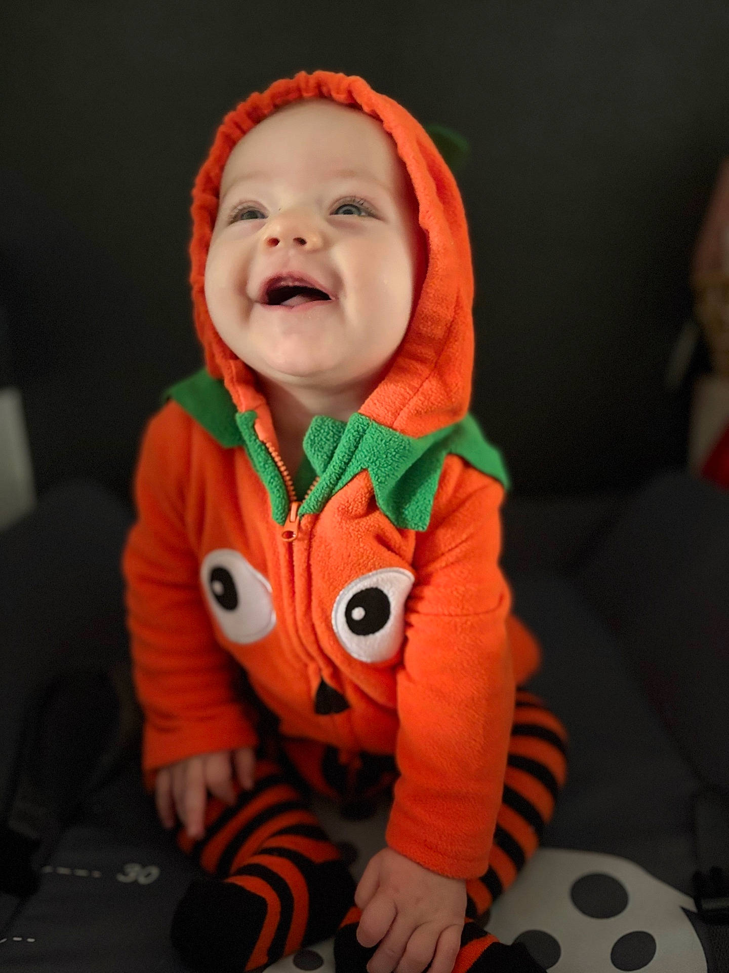 Myla participe au concours pour gagner de l'argent avec cette photo : baby, black_background, child, costume, cute, face, feet, hands, happy, hooded_jacket, indoor, infant, orange_clothing, portrait, pumpkin_costume, seasonal, sitting, smiling, soft_texture, striped_socks