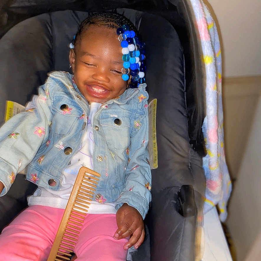 Rosyana is registered to the contest to win money with this photo: accessory, baby, beaded_hair, braids, car_seat, child, clothing, comb, cute, denim_jacket, furniture, happy, indoor, joyful, person, pink_pants, portrait, seat, smiling, toddler