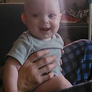 Waylon joined the competition — help win amazing prizes! baby, infant, child, smiling, happy, portrait, face, indoor, home, being_held, adult_hand, blanket, checkered_blanket, clothing, t_shirt, seated, couch, close_up, family, photography