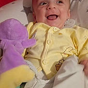 Eden a rejoint le concours — aidez-le/la à gagner de superbes lots ! baby, smiling, yellow_onesie, stuffed_toy, purple_toy, blanket, red_fish, happy, infant, portrait, child, cute, indoor, cozy, soft_toy, bedtime, face, person, playful, comfort