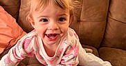 Oaklan joined the competition — help win amazing prizes! toddler, child, smiling, pigtails, pajamas, couch, brown_furniture, happy, indoor, climbing, cute, person, face, hair_bows, young_child, playful, cozy, home, casual, fun