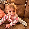 toddler, child, smiling, pigtails, pajamas, couch, brown_furniture, happy, indoor, climbing, cute, person, face, hair_bows, young_child, playful, cozy, home, casual, fun