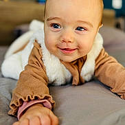 Ninon a rejoint le concours — aidez-le/la à gagner de superbes lots ! baby, child, smiling, blue_eyes, face, hand, clothing, bed, soft_texture, indoor, portrait, cute, infant, warm_colors, cozy, young_child, expression, person, closeup, playful