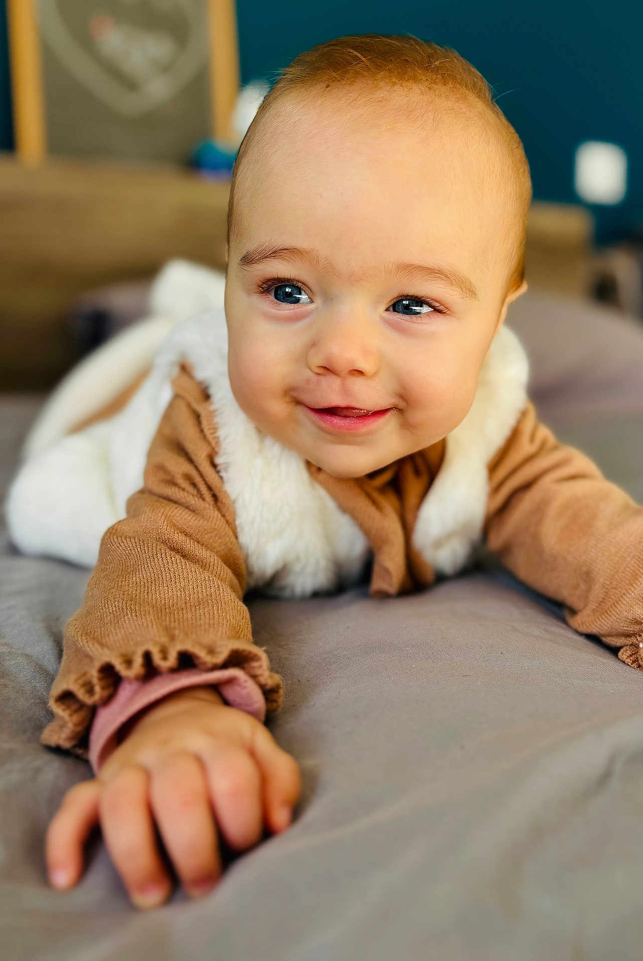 Ninon a rejoint le concours — aidez-le/la à gagner de superbes lots ! baby, child, smiling, blue_eyes, face, hand, clothing, bed, soft_texture, indoor, portrait, cute, infant, warm_colors, cozy, young_child, expression, person, closeup, playful