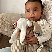 Isaïah participe au concours pour gagner de l'argent avec cette photo : baby, infant, child, plush_toy, stuffed_animal, sofa, blanket, knit_pants, socks, hands, face, portrait, indoors, cozy, curly_hair, cute, toy, cuddle, seated, neutral_background