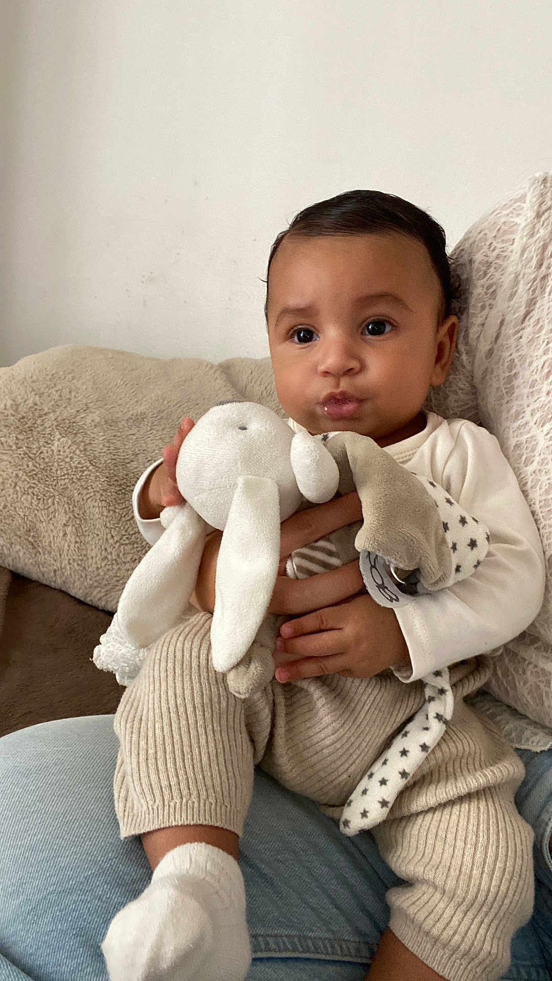 Isaïah participe au concours pour gagner de l'argent avec cette photo : baby, infant, child, plush_toy, stuffed_animal, sofa, blanket, knit_pants, socks, hands, face, portrait, indoors, cozy, curly_hair, cute, toy, cuddle, seated, neutral_background