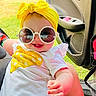 baby, child, sunglasses, yellow_headwrap, white_shirt, car_door, grass, smiling, happy, outdoor, casual, infant, sunlight, portrait, cute, fashion_accessory, seat, hand, candid, summer