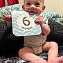 baby, infant, six_months, milestone_card, smiling, sitting, blanket, pillow, indoors, cute, child, face, hands, feet, clothing, diaper, happy, portrait, playful, home