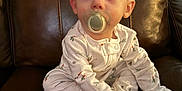 Dawson is registered to the contest to win money with this photo: baby, pacifier, pajamas, child, infant, leather_chair, sitting, indoor, cute, young_child, person, small_hands, curious, face, head, eyes, furniture, home, comfort, cozy