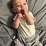 baby, child, infant, smiling, hand, pacifier, clothing, shorts, shirt, blanket, bed, cute, happy, lying_down, face, skin, person, indoors, soft, relaxed