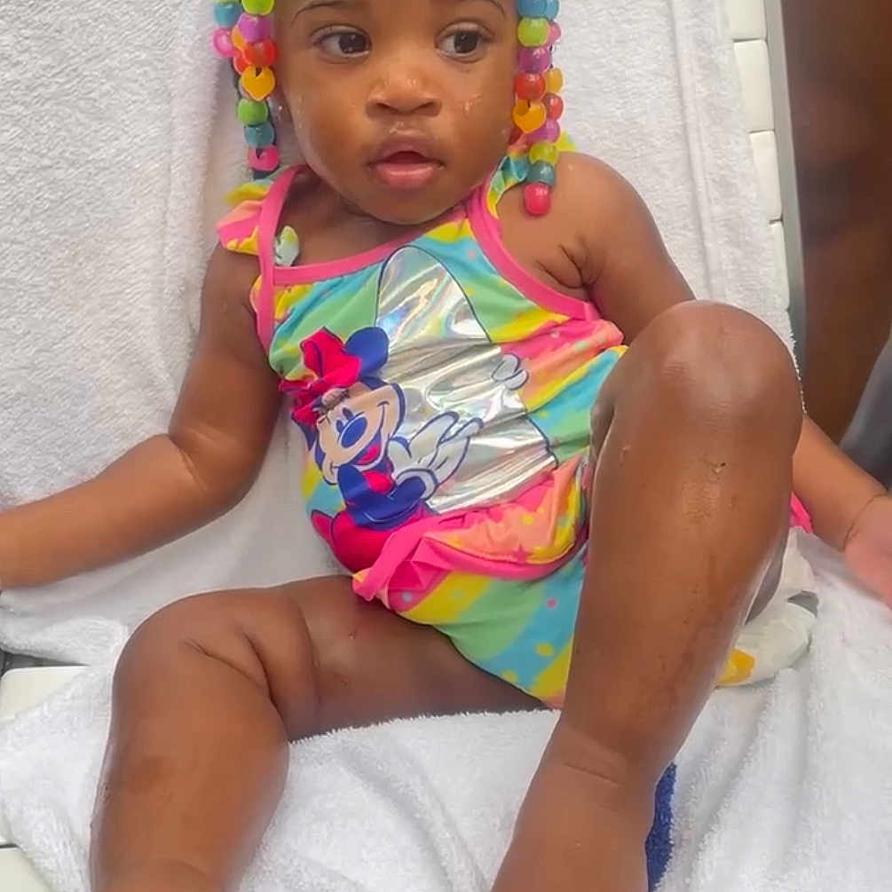 Privy is registered to the contest to win money with this photo: beads, braids, bright_colors, child, colorful, cute, feet, legs, minnie_mouse, outdoor, person, playful, relaxed, sitting, skin, summer, swimsuit, toddler, towel, water_droplets